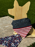 Reversible over collar dog bandana. This bandana includes a navy blue fabric with white stars and red and white stripes.  The reverse pattern features cartoon dogs and patriotic stars.